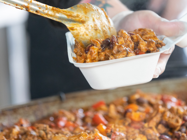 Someone serving up a big pan meal into a white box.