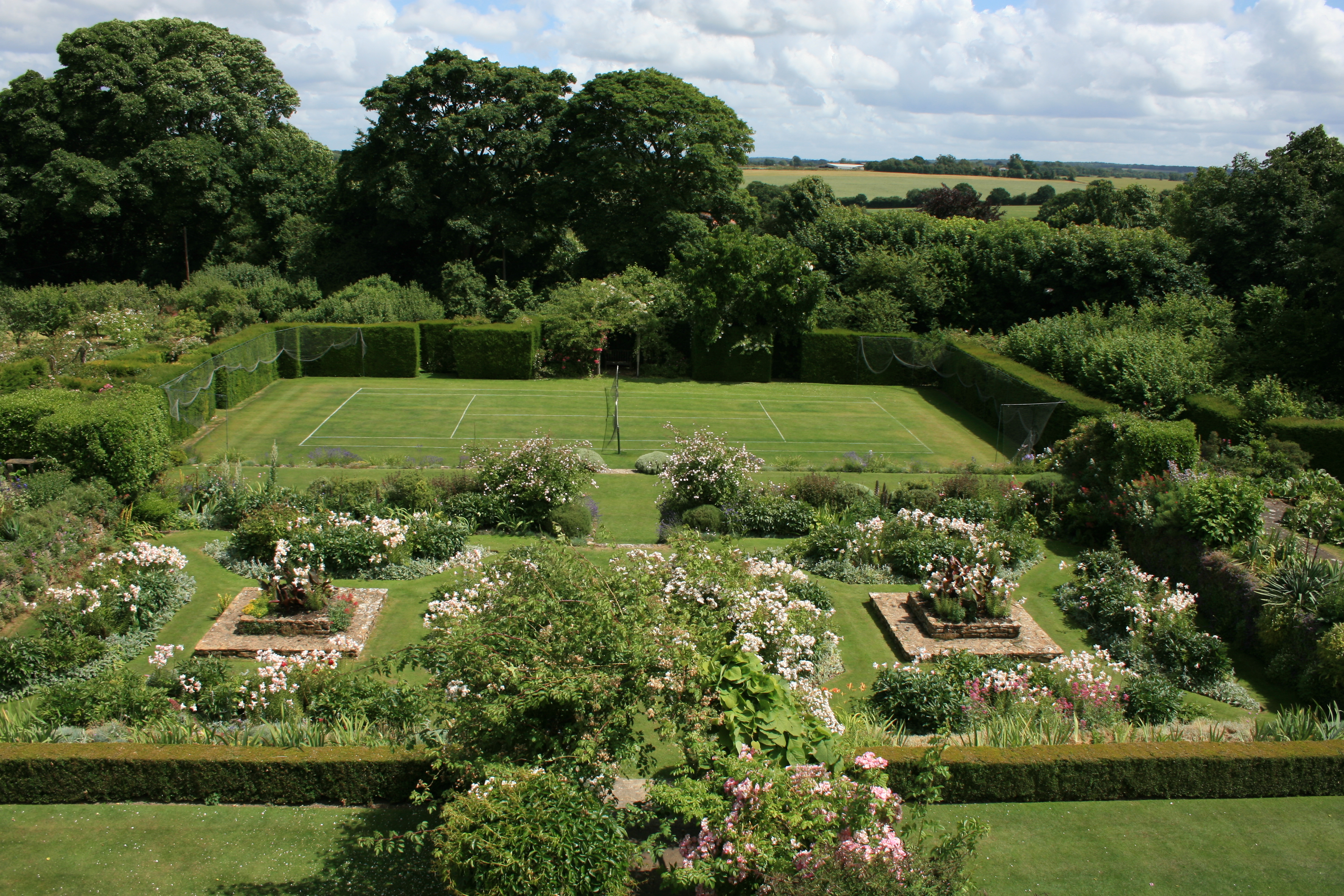 A photograph of an ornate hisorical restored garden, origins date back to 1908.  The drops in levels to the Rose garden, Bowling and Tennis lawns are supported by dry-stone walls which Miss Jekyll planted to give the effect of vertical flower-beds; those plants fill the areas with colour from late February onwards.