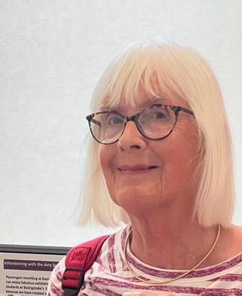 A female with glasses smiles and looks at the camera. You can see she is wearing a red and white striped T shirt.