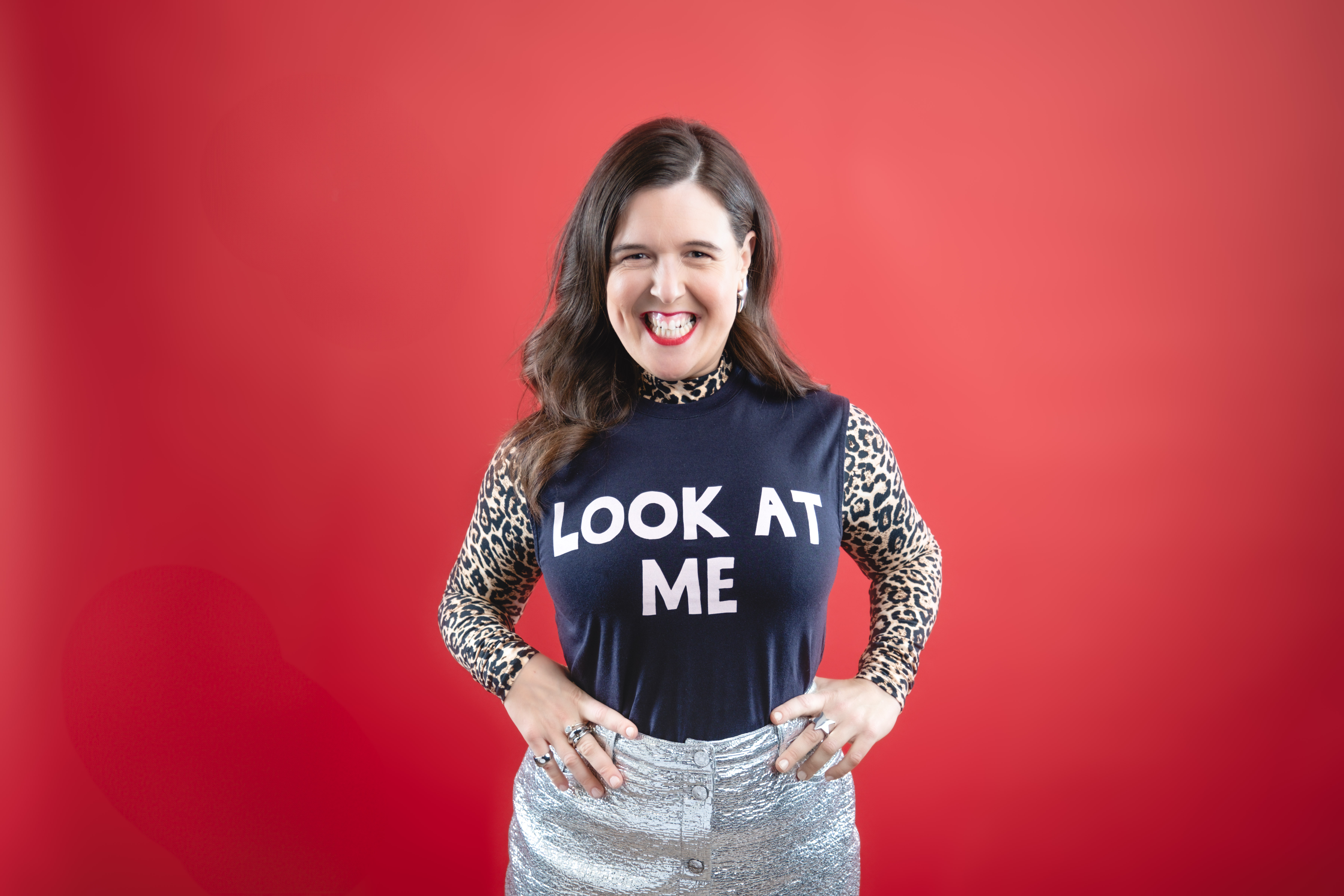 A female stands against a red background wearing a top that says Look at Me.