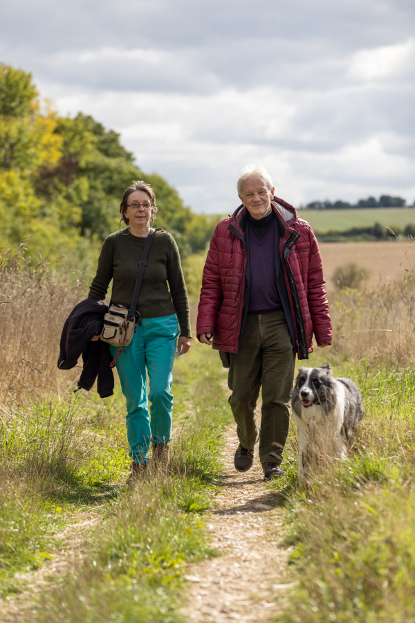Two people and their dog are walking in the outdoors.