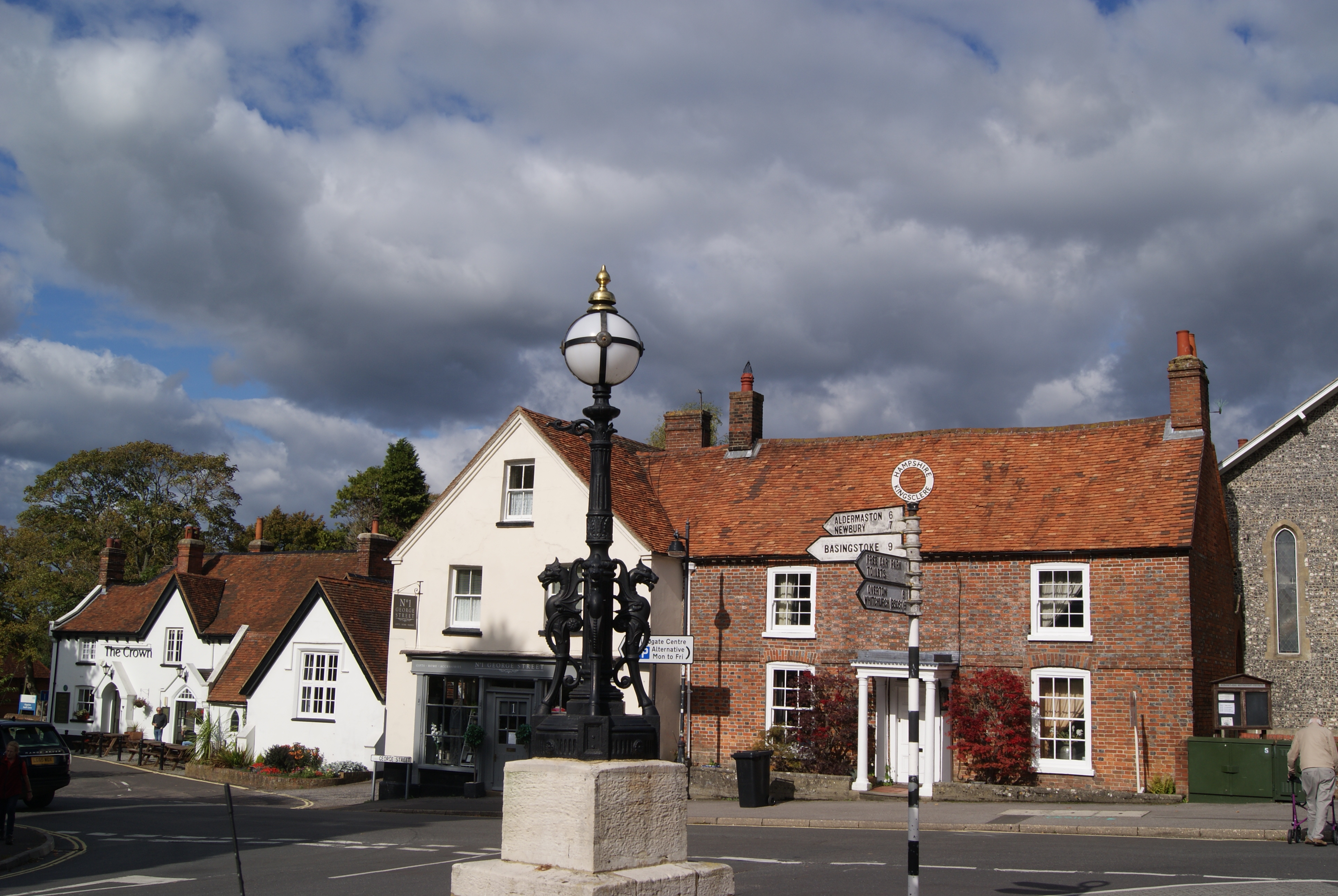 Kingsclere Village Square. A lamppost sits on a concrete block in the center of a roundabout. Houses surround the road.