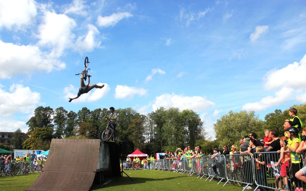 A man does a trick on a bmx bike high in the air above a ramp. A crowd watches on.