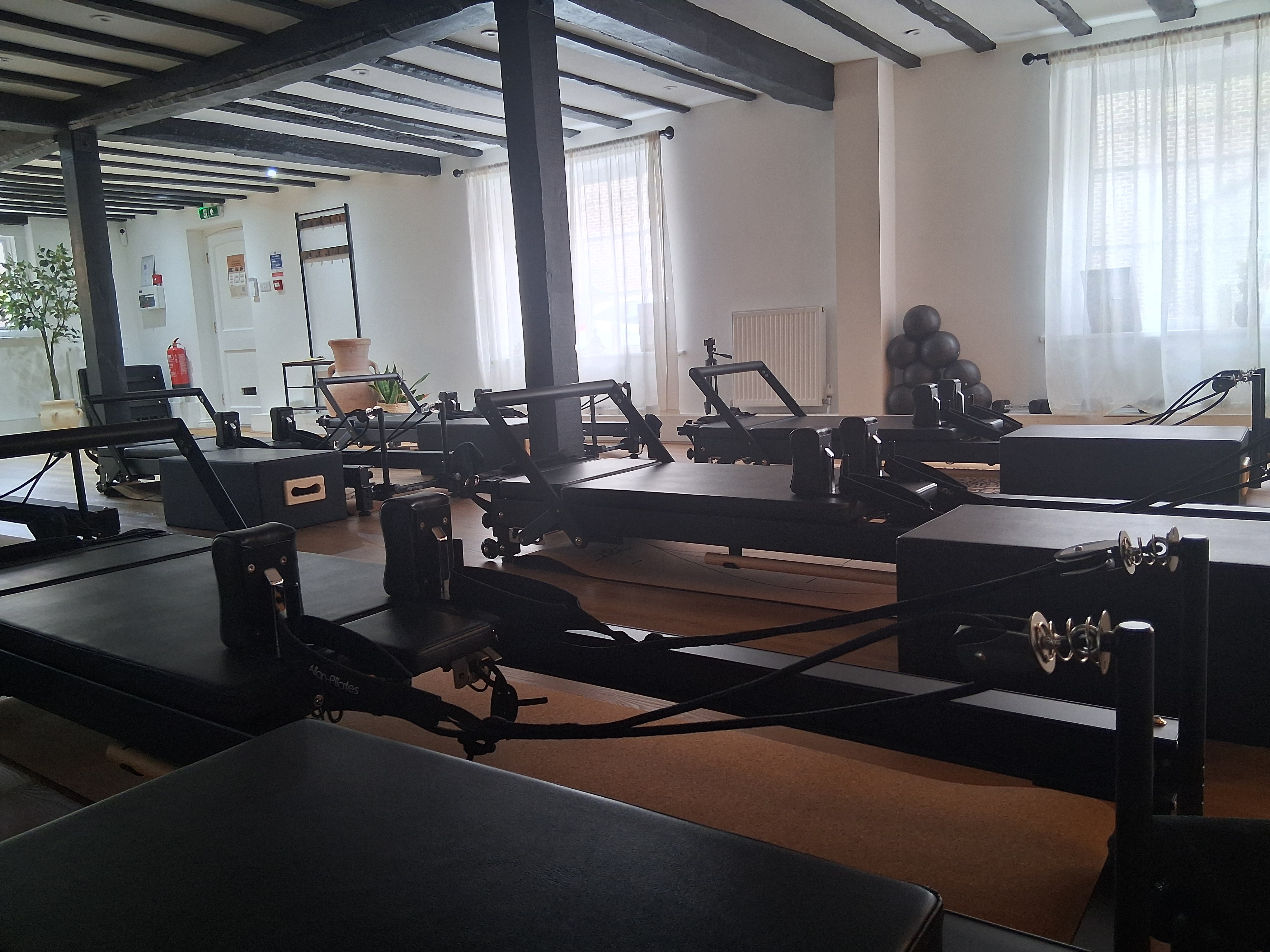 A studio that has a wooden beamed ceiling. You can see lots of reformer machines in the picture.