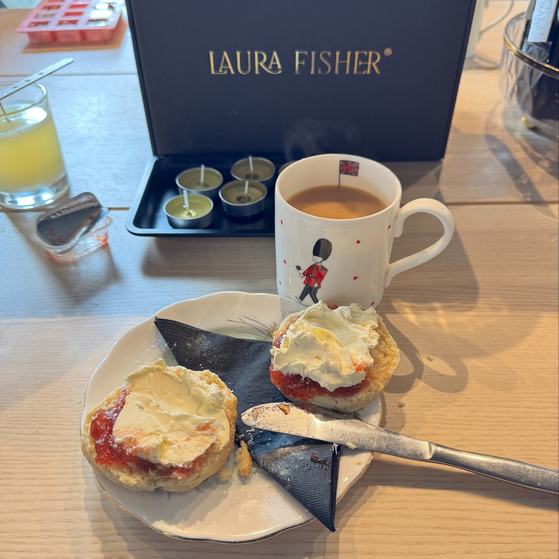 A Laura Fisher sign with some tea lights in front. Then a mug of tea and a plate with scones.