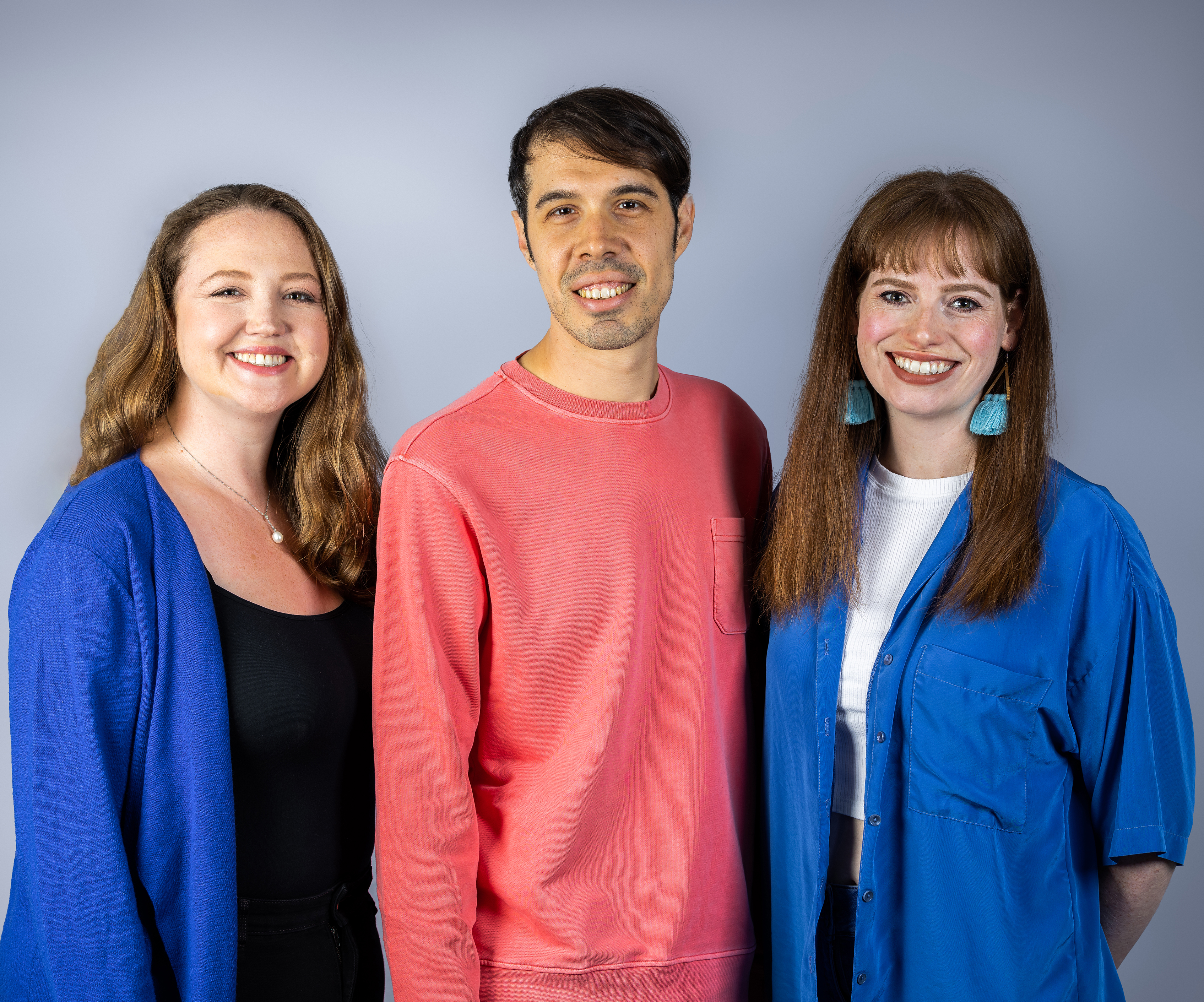 Ilario Ferrari Tri. Two women, wearing dark blue jackets are smiling and standing either side of a man in a red jumper with short brown hair.