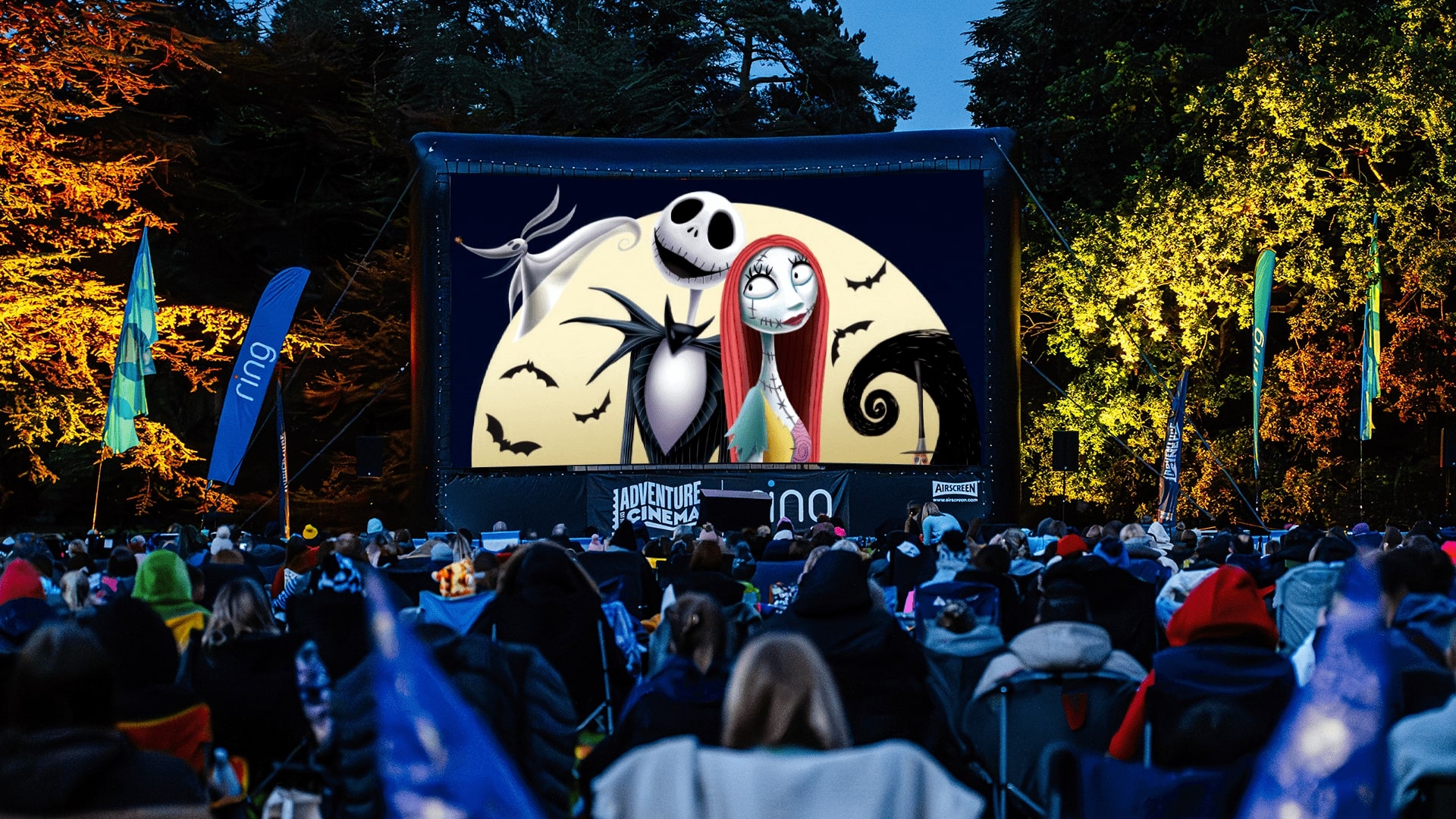 A ghost, a skeleton bride and a skeleton groom on a screen with people watching.