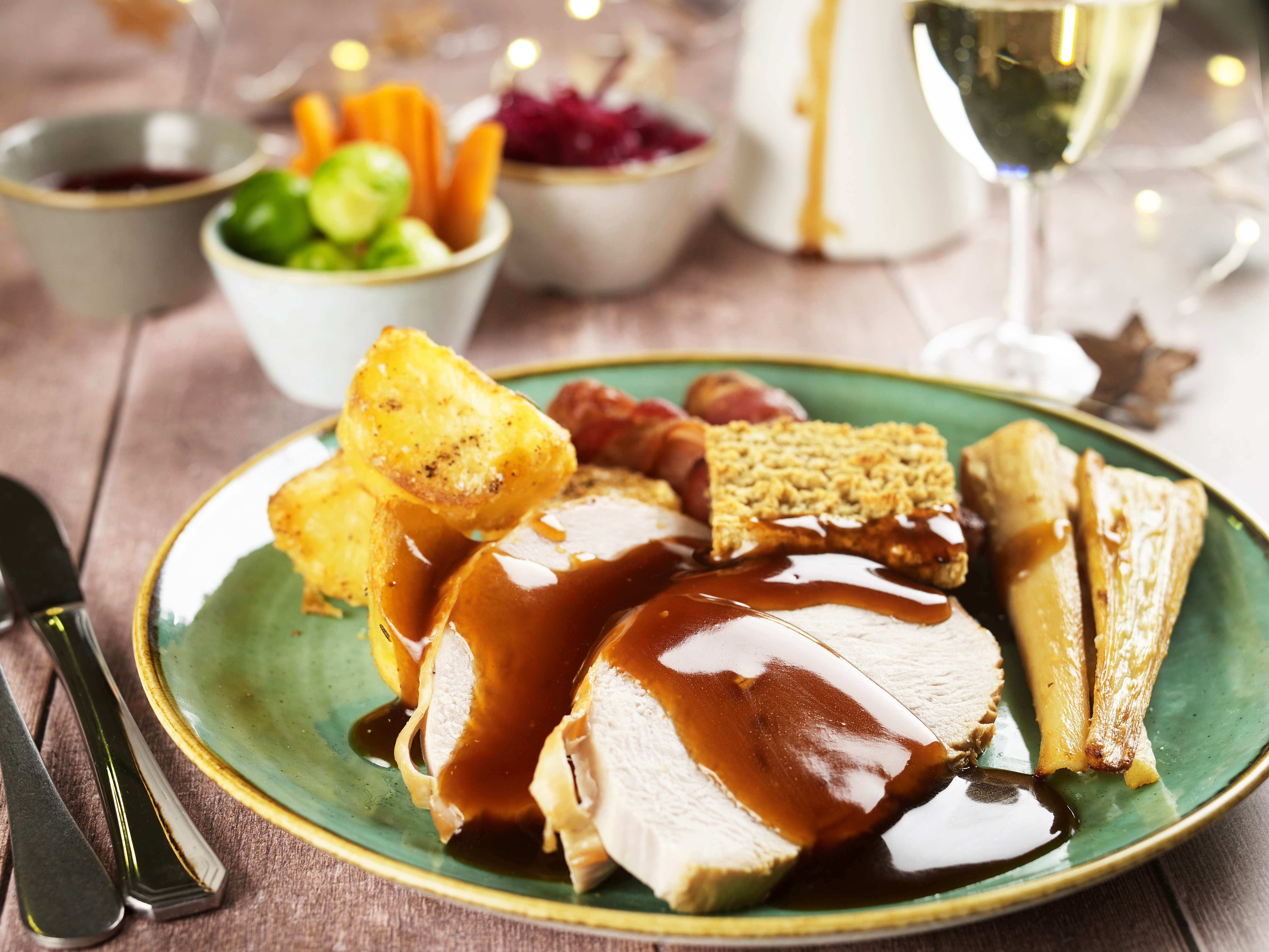 Chicken breast on a dark green plate. There is roast potatoes, gravy and pigs in blankets.