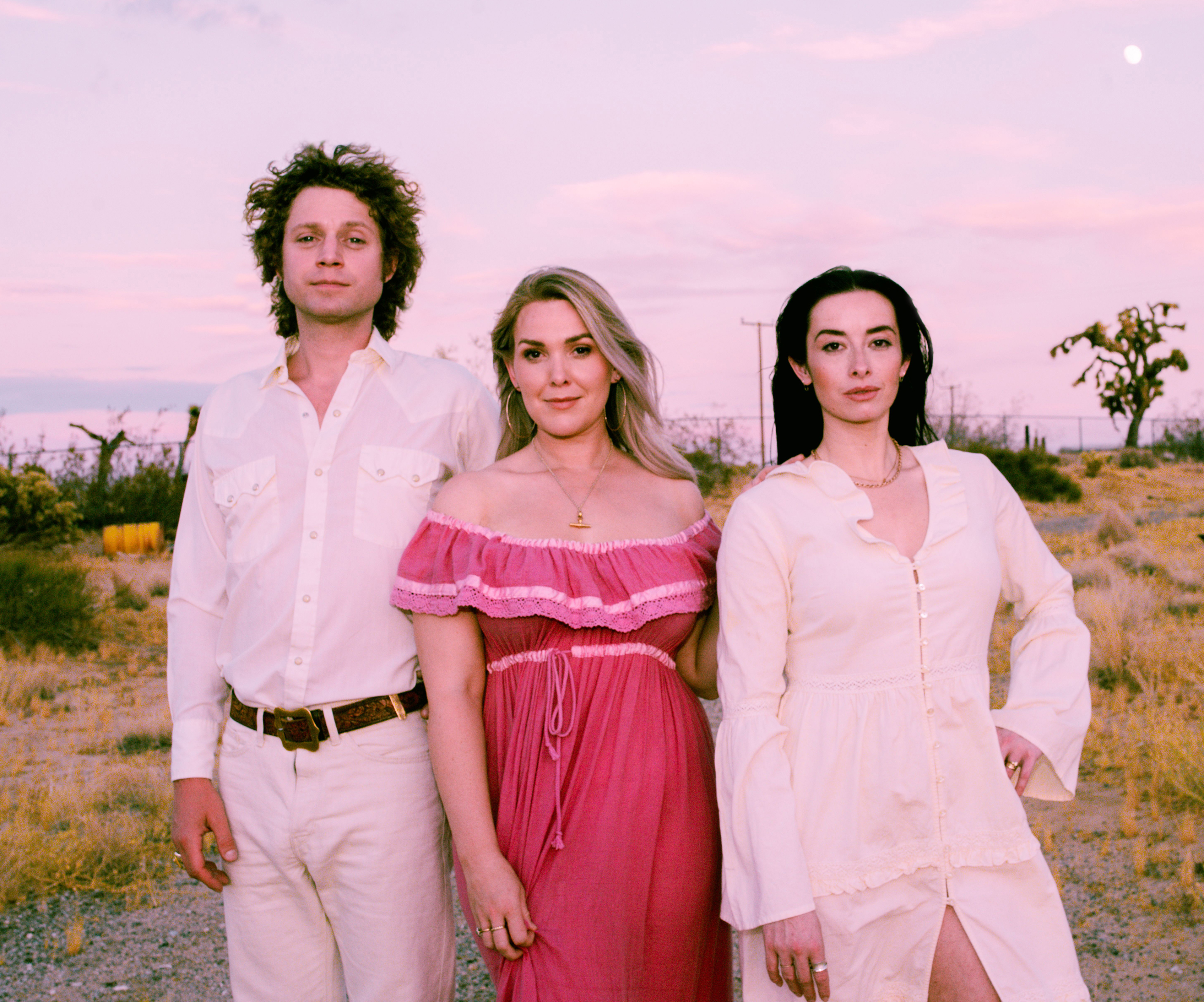 Three people are stood side by side outside. They are looking at the camera and smiling.