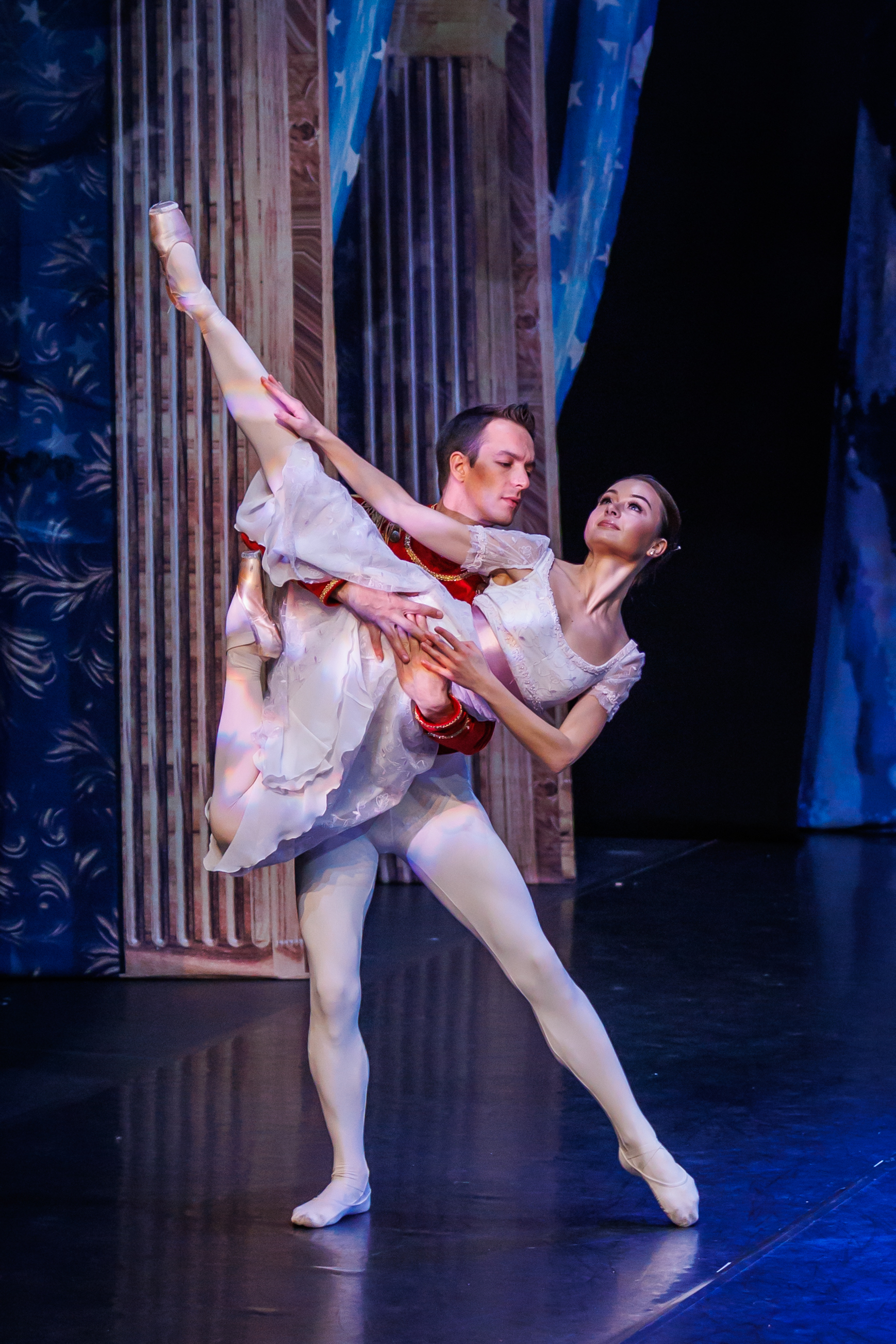 A female ballerina is held in a pose off the ground by a male ballerina