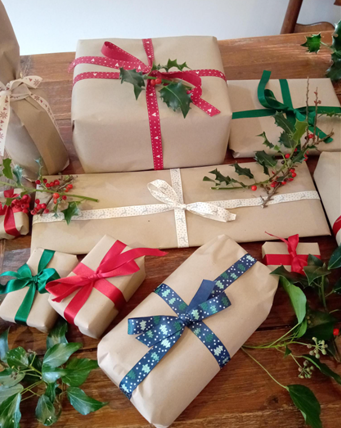 A pile of Christmas presents wrapped in brown paper with colourful reusable ribbons.
