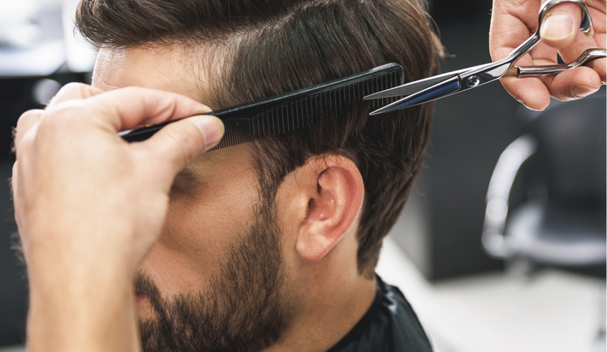Image showing the profile of a man's  face and a barber's hands with a comb and scissors cutting his hair