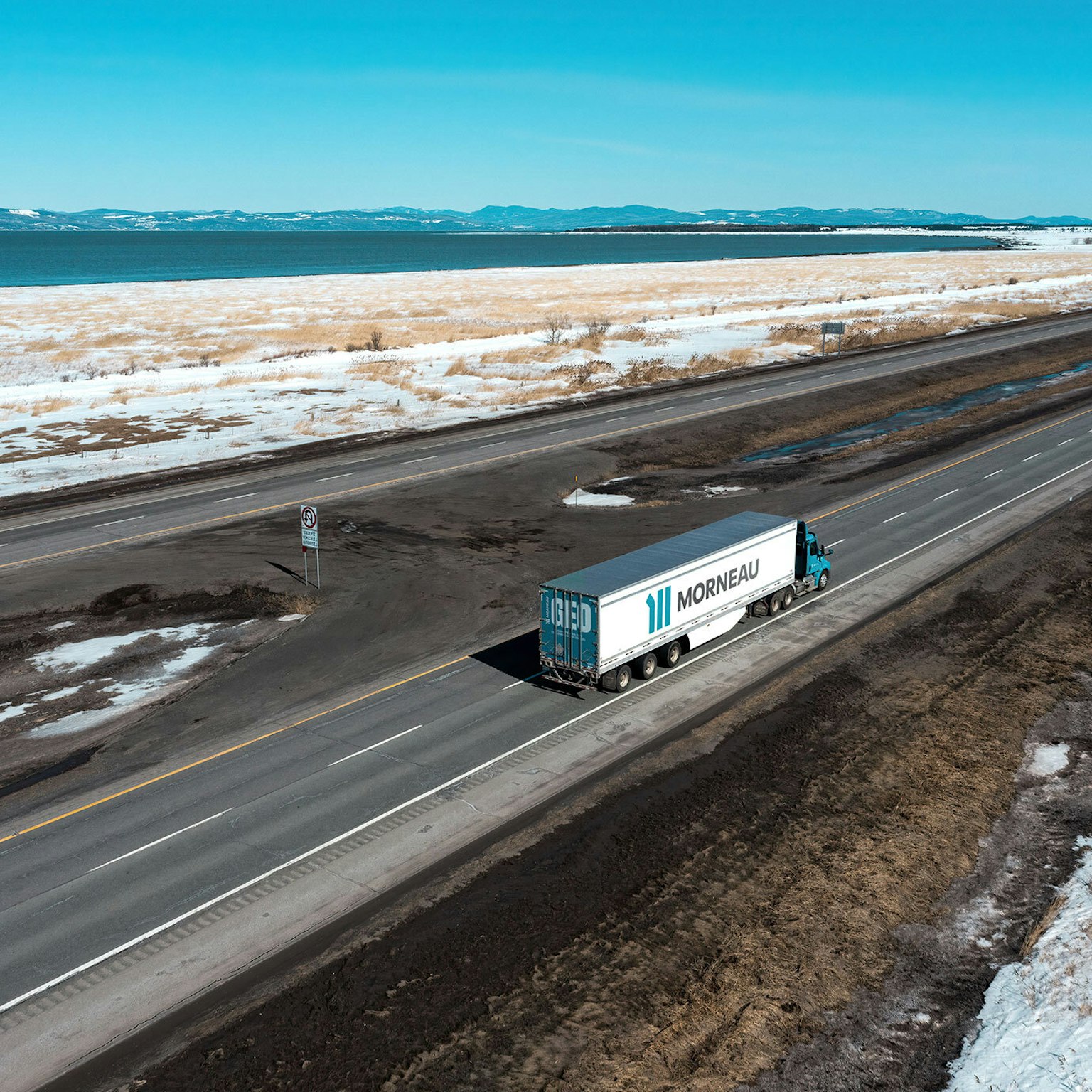 Un camion du Groupe Morneau, en vue aérienne, parcourant les routes du Québec en hiver.