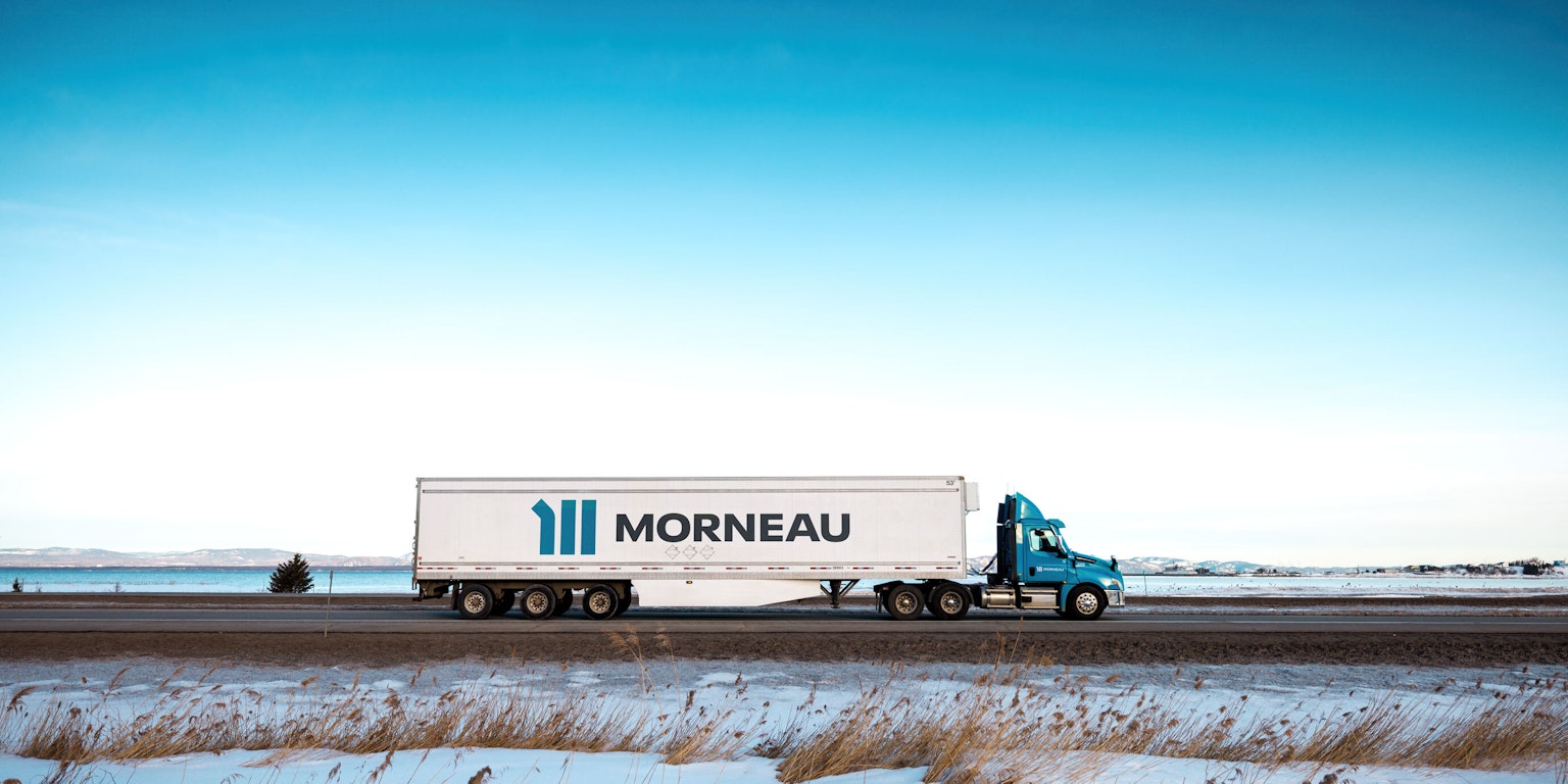 Un camion du Groupe Morneau, en vue aérienne, parcourant les routes du Québec en hiver.