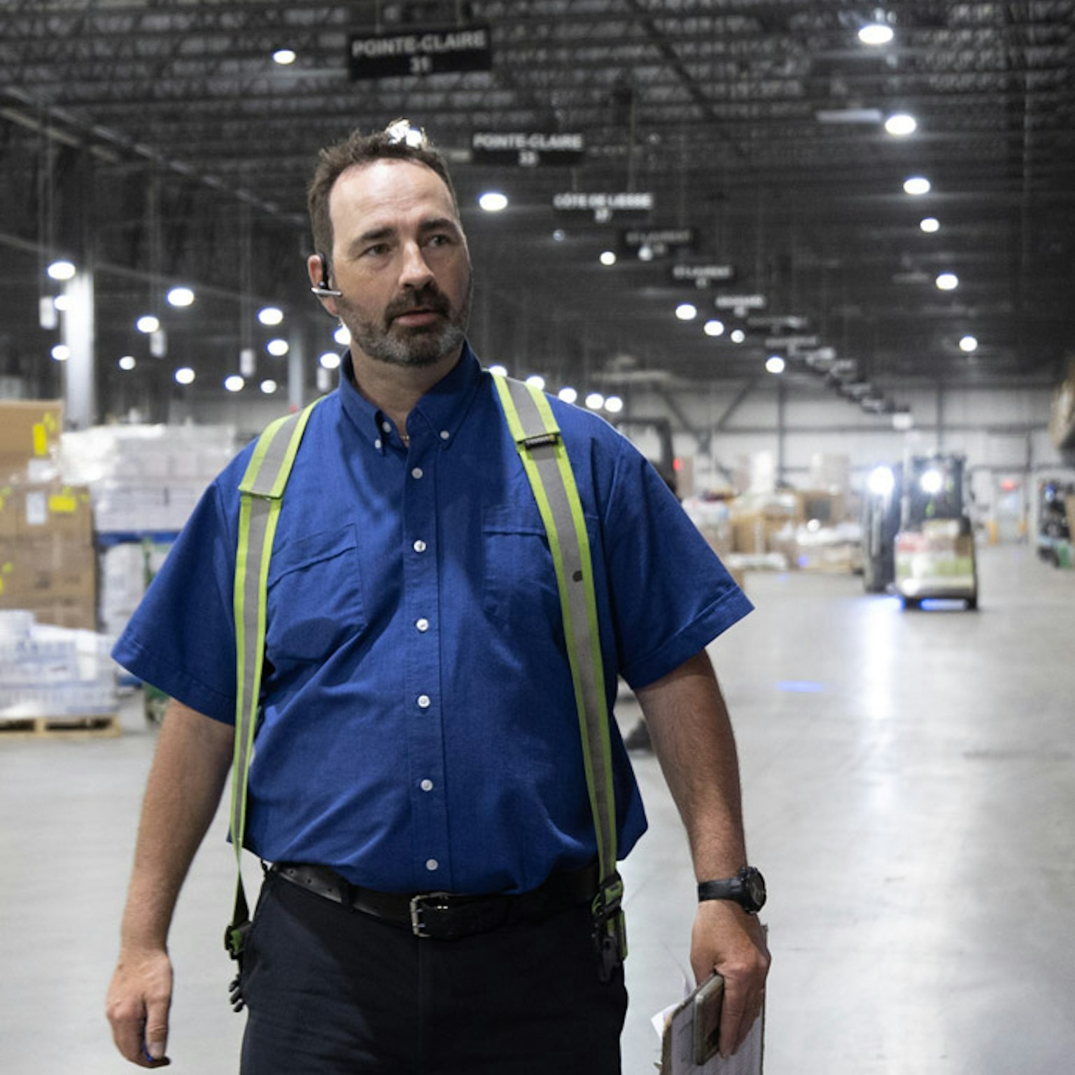 Contremaître avec gilet de sécurité jaune se déplaçant dans un entrepôt de logistique pour valider la répartition des marchandises.