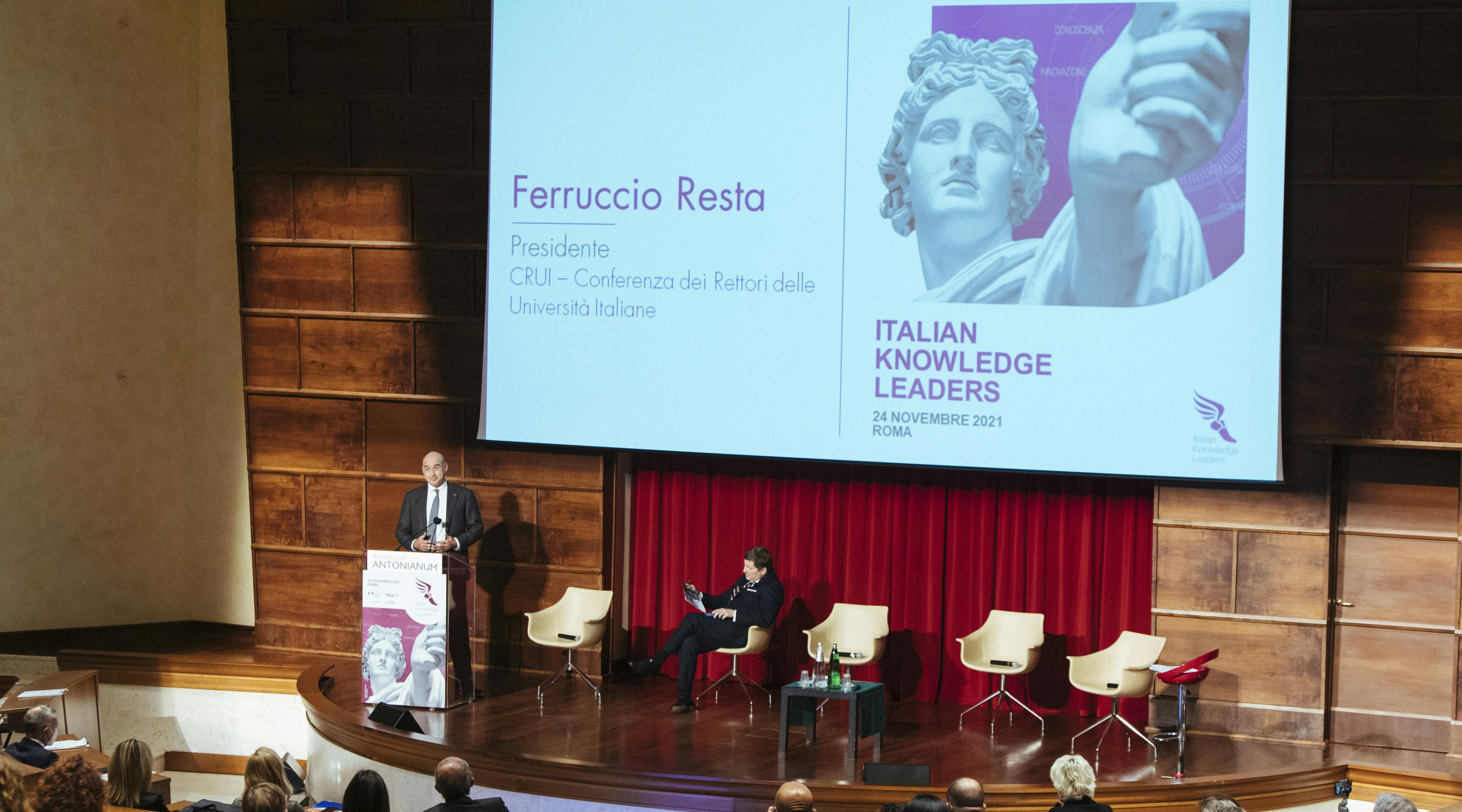 presidente crui ferruccio resta interviene sul palco con microfono e schermo all'evento italian knowledge leaders proiezione