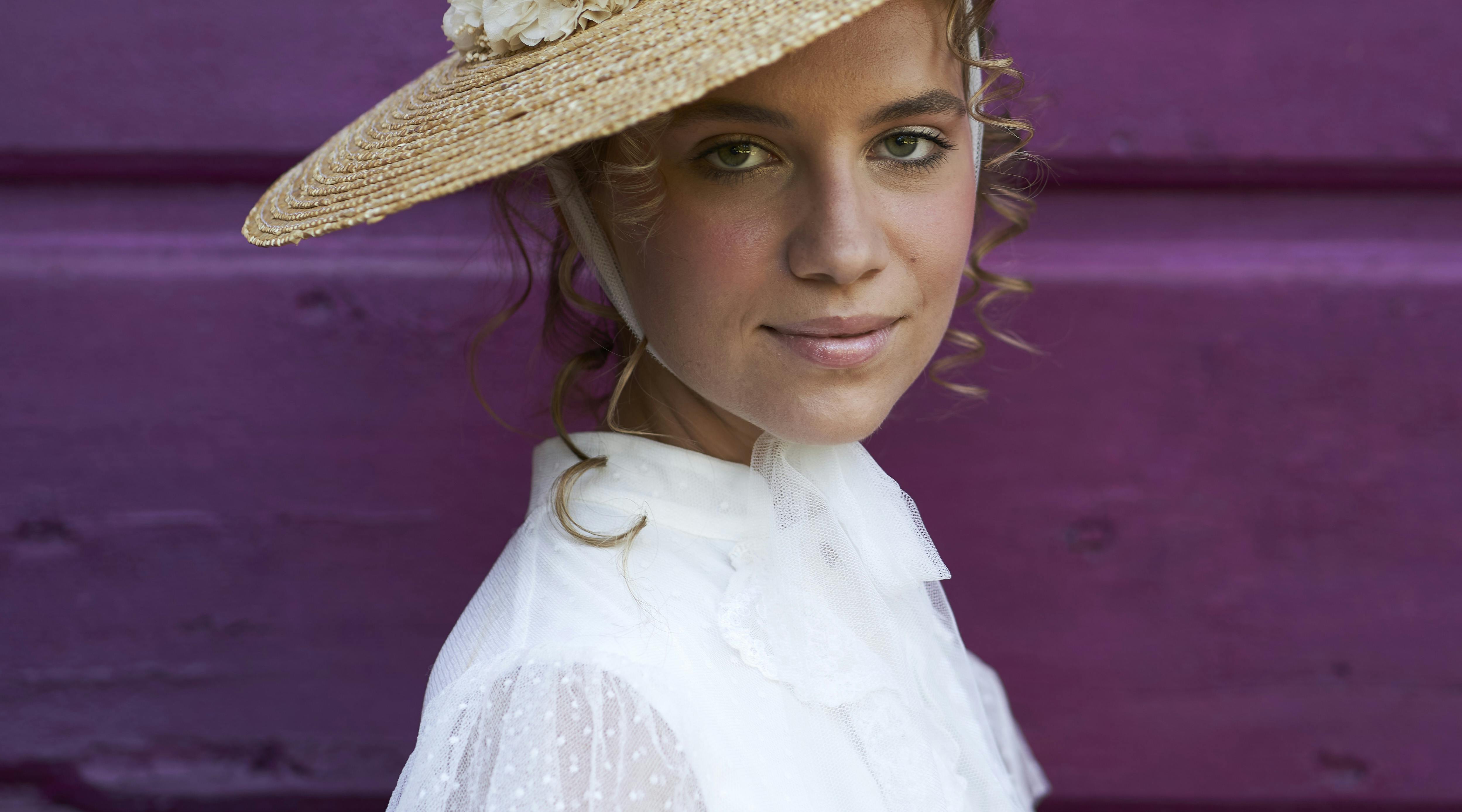 bride dressed as bride wearing a hat in front of a purple wooden door