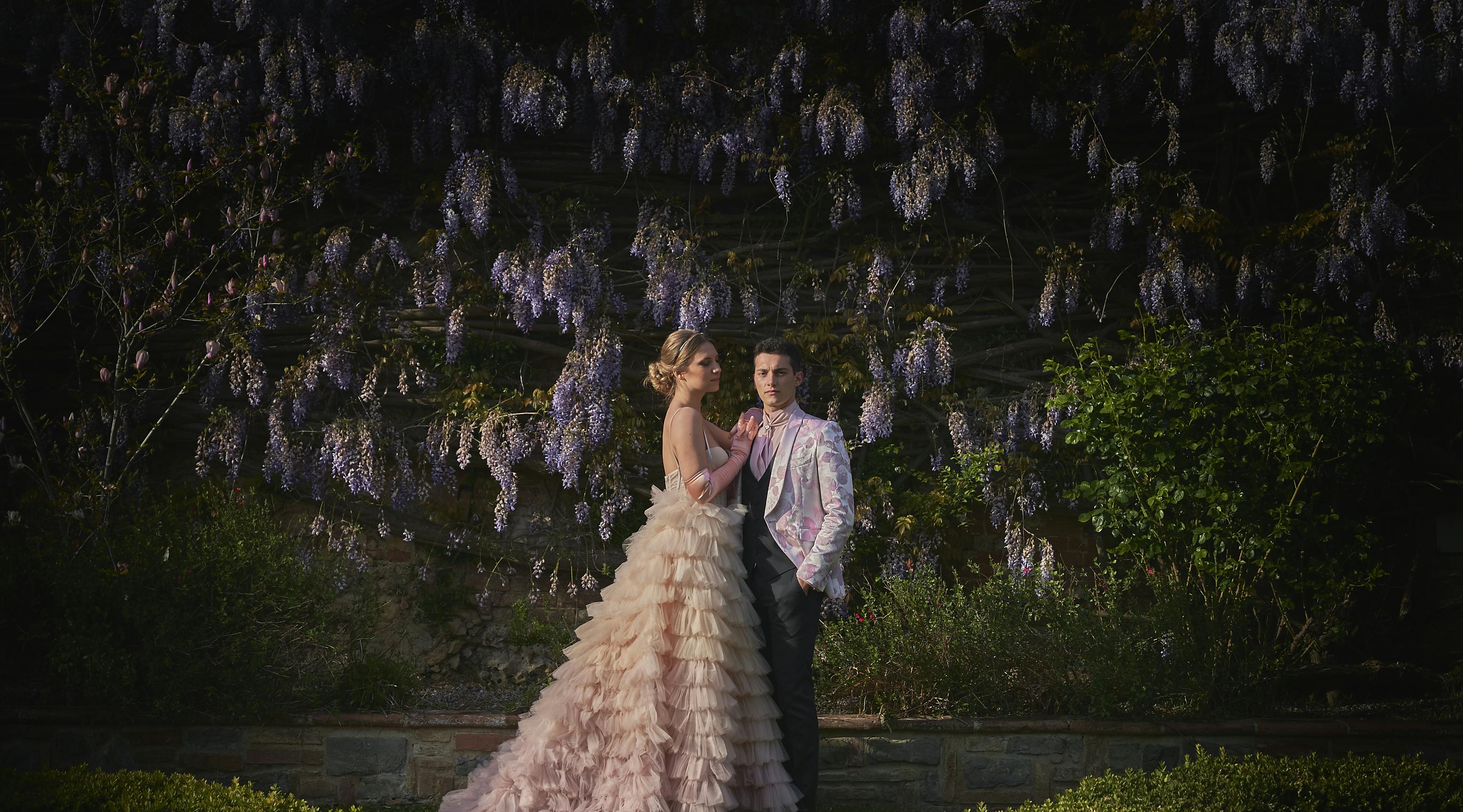 coppia di sposi in campagna con abiti di alta moda davanti a glicini