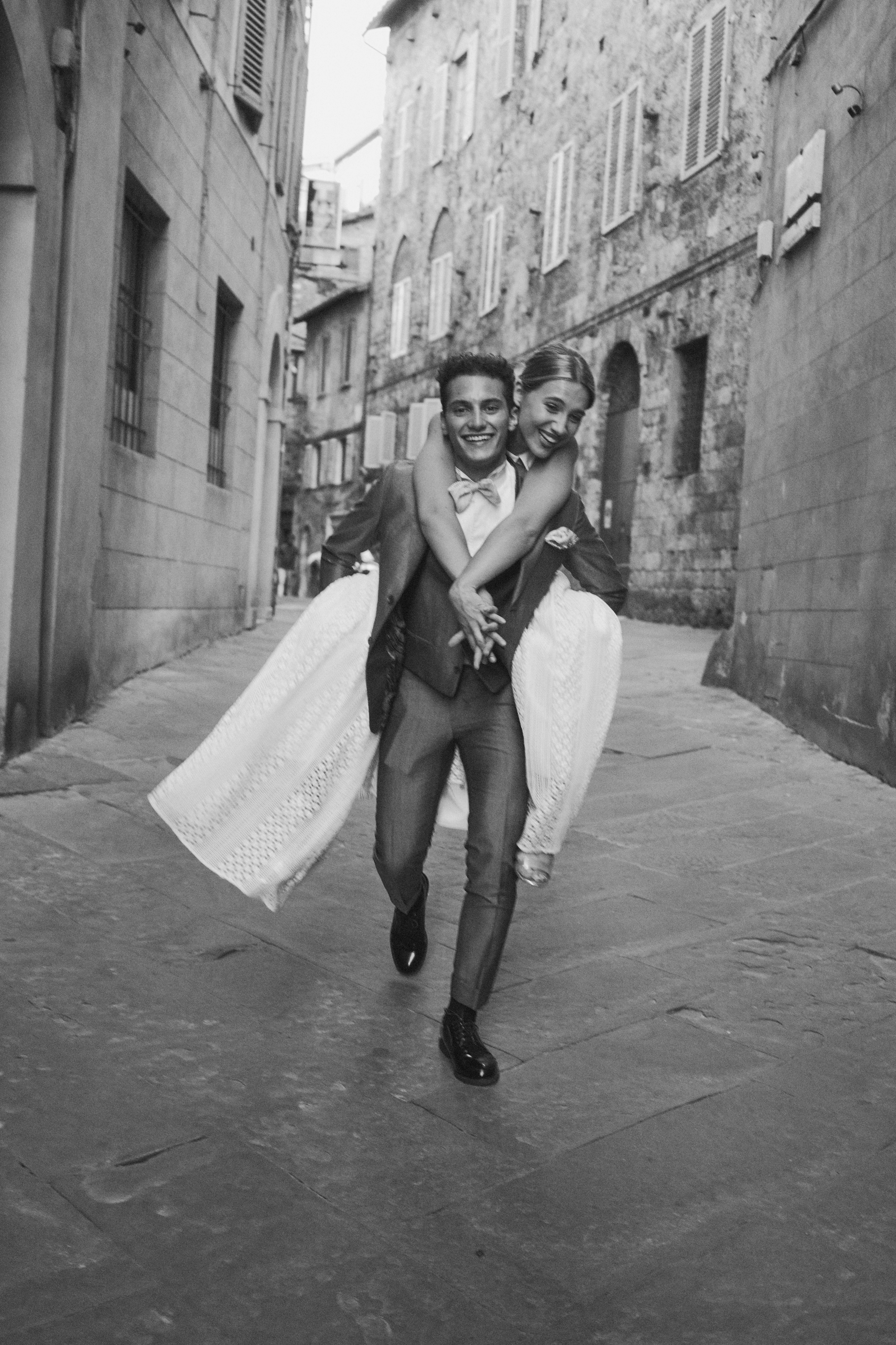 Bride and groom with groom carrying the bride on his back on the streets of siena