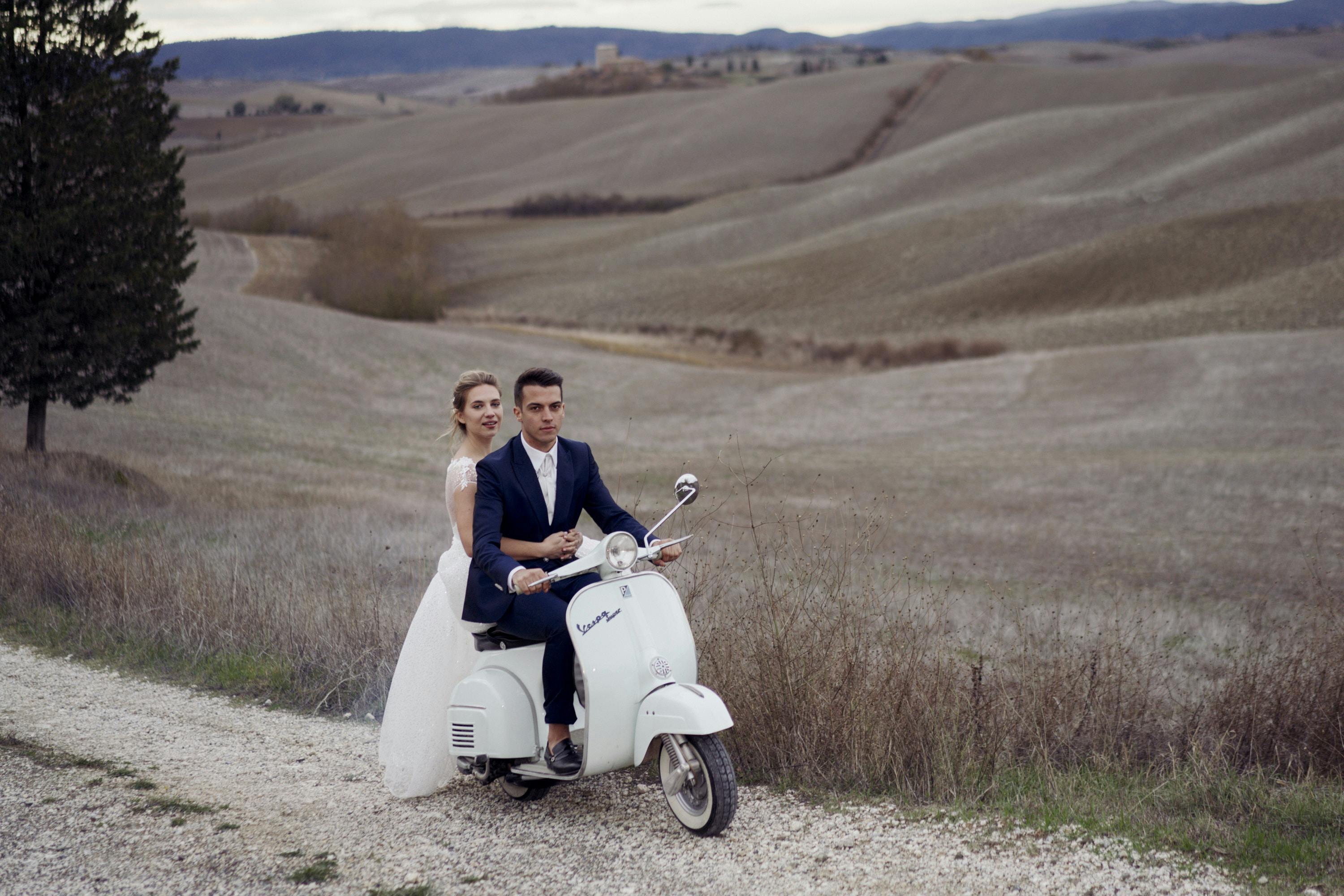 bride and groom on a vintage vespa on a countryside road near siena with fields in the background