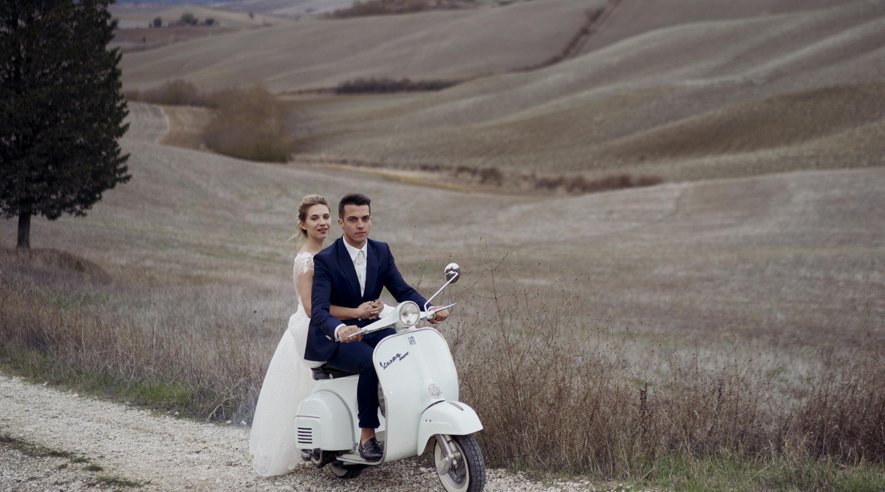 bride and groom on a vintage vespa on a countryside road near siena with fields in the background