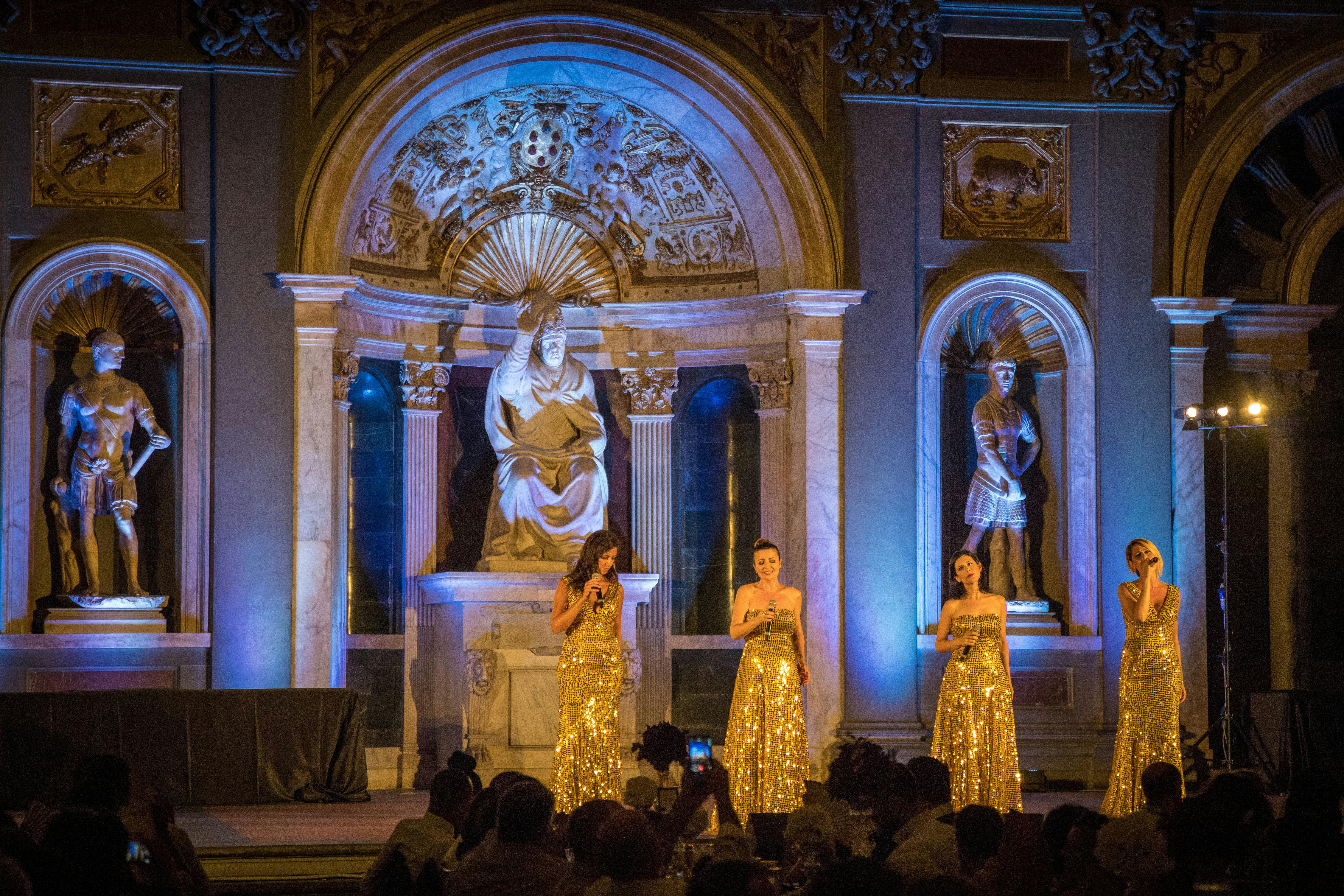 4 donne cantano su un palco nel salone de'cinquecento a firenze indossando vestiti dorati