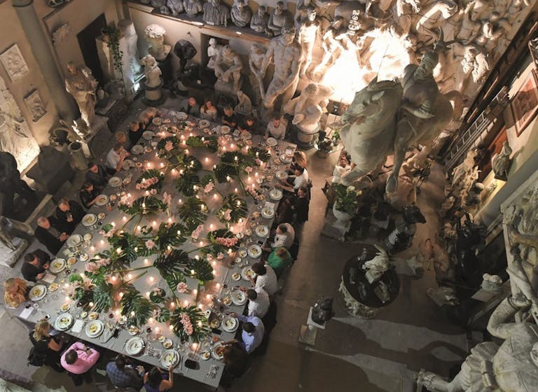 cena di gala in un palazzo storico con statue e piante in mezzo al tavolo