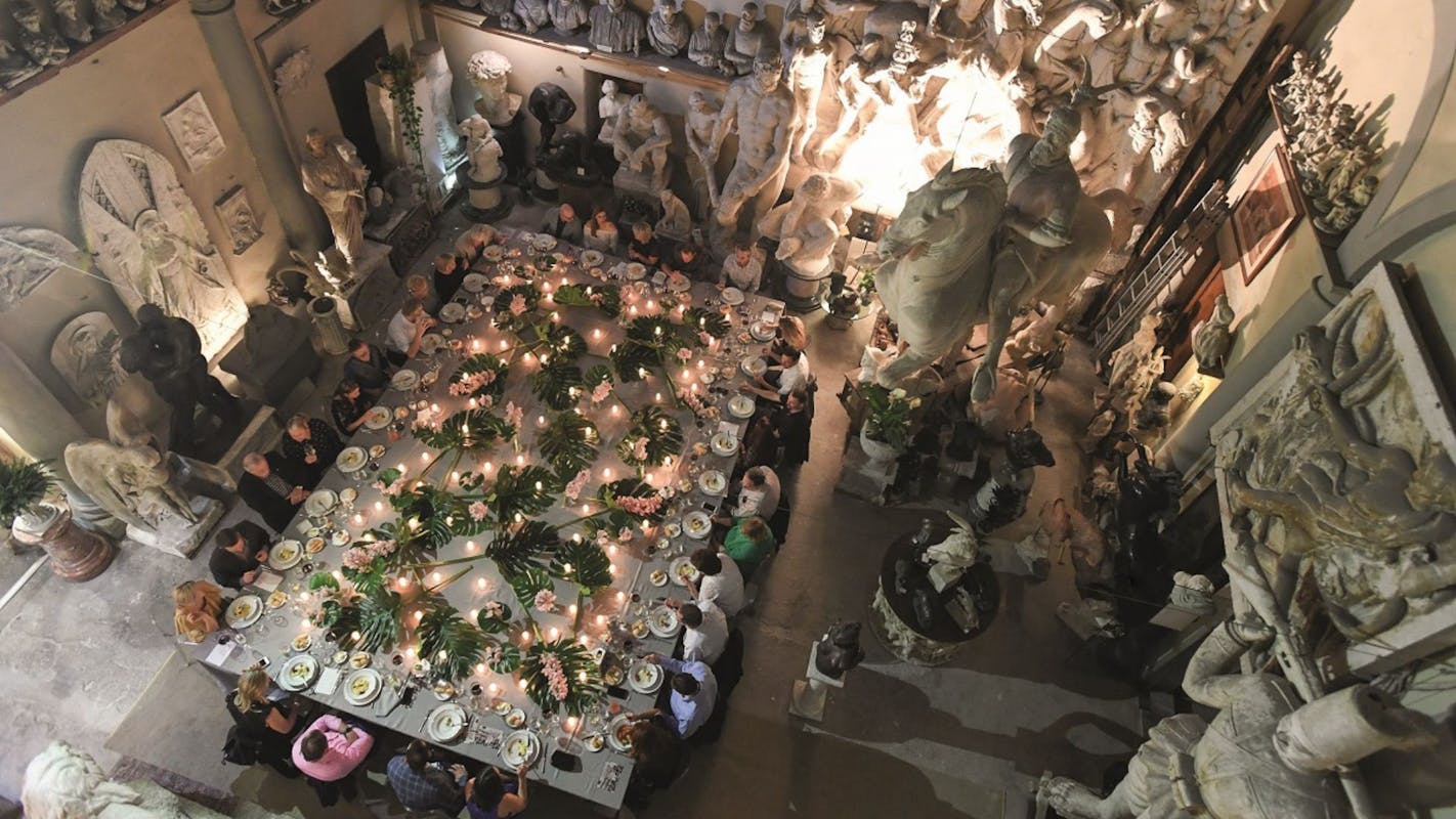 cena di gala in un palazzo storico con statue e piante in mezzo al tavolo