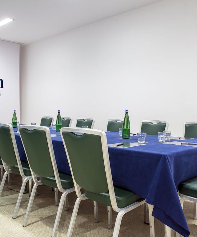 Sala riunioni con tavolo blu, sedie verdi e pareti bianche