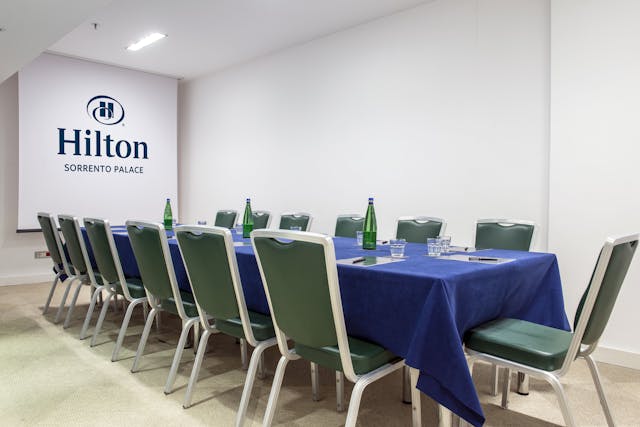 Sala riunioni con tavolo blu, sedie verdi e pareti bianche