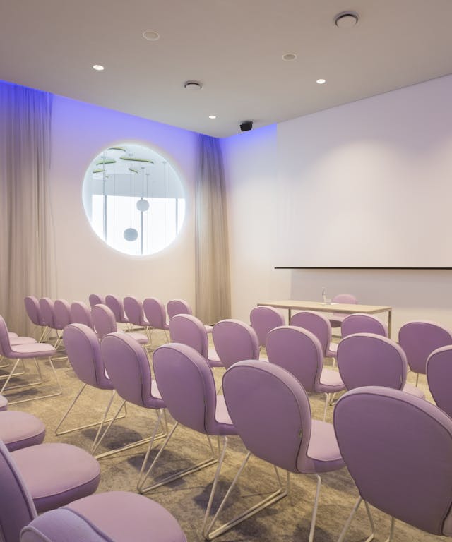 Sala riunioni con sedie rosa e schermo bianco