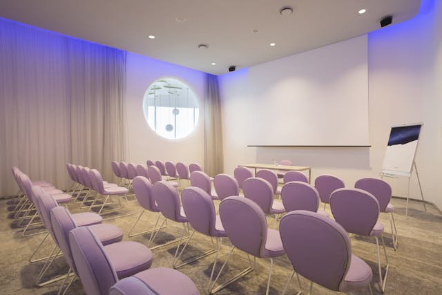 Sala riunioni con sedie rosa e schermo bianco
