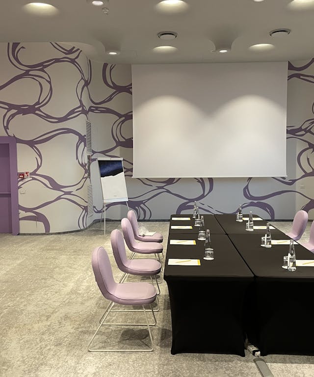 Sala riunioni con tavolo nero, sedie rosa e pareti bianche