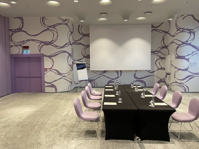Sala riunioni con tavolo nero, sedie rosa e pareti bianche
