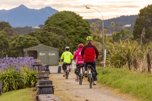 Three cyclists on a trail with mountains in the background.