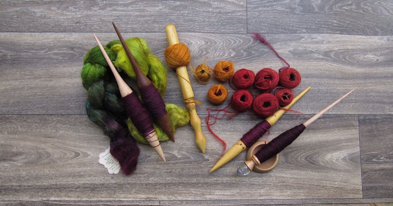 An array of spindles, fiber, and yarn against a wooden background.