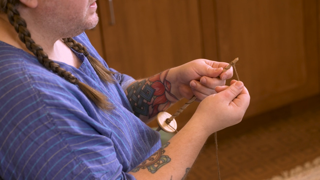 instructor holding a drop spindle and showing how to add a leader