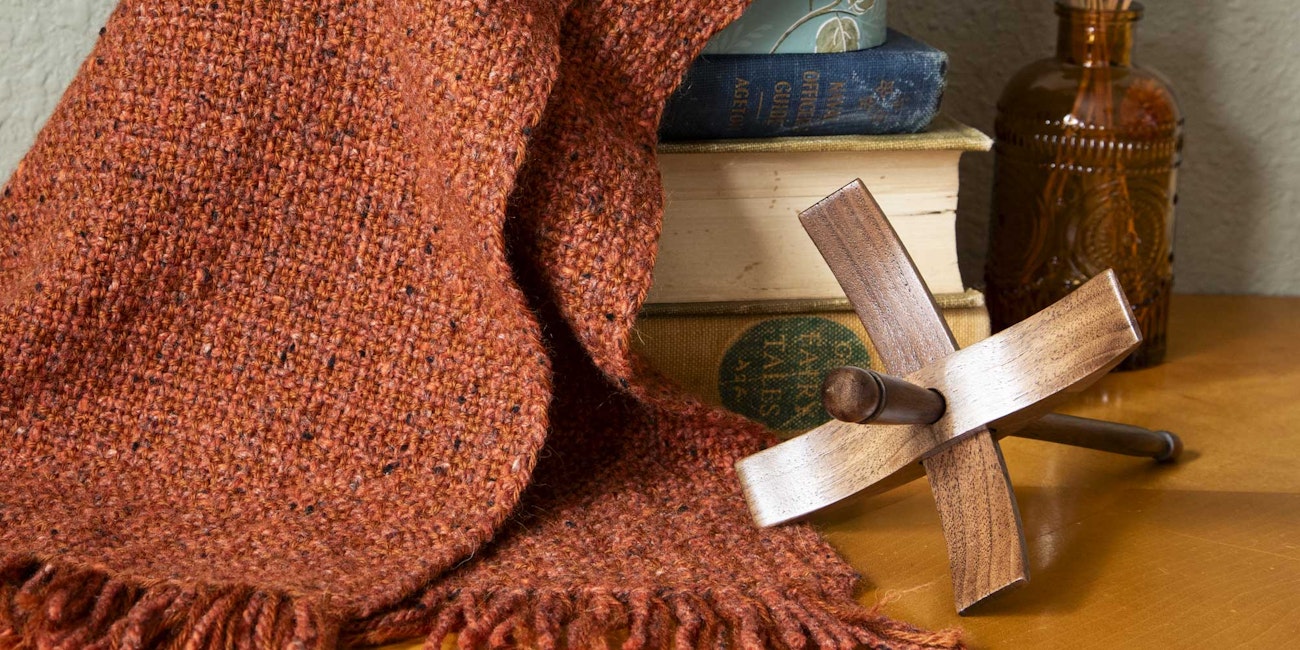 A reddish-brown scarf is draped over a stack of old books. Next to it rests a wooden spindle.