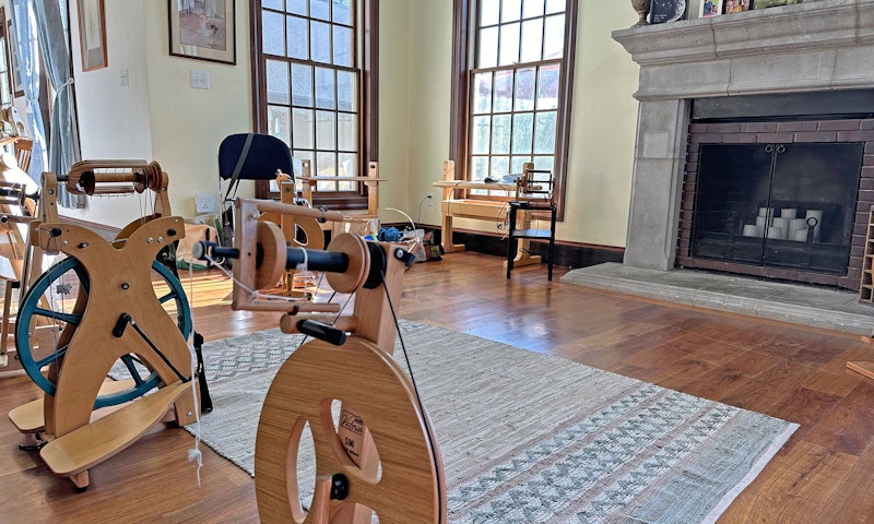 sunny room with spinning wheels, looms, and fireplace