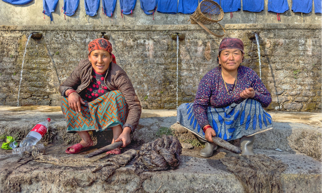 Two Nepali women pound giant nettle before spinning it into thread