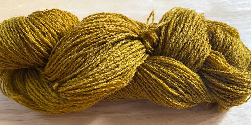 A brassy yellow skein of yarn rests on a wooden surface.