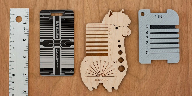 A metal ruler, a metal yarn gauge, an alpaca-shaped yarn gauge, and a 3D printed yarn gauge on a wood surface.