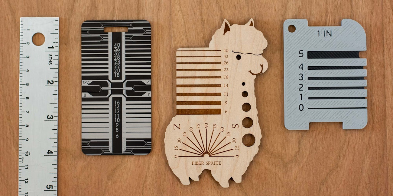 A metal ruler, a metal yarn gauge, an alpaca-shaped yarn gauge, and a 3D printed yarn gauge on a wood surface.