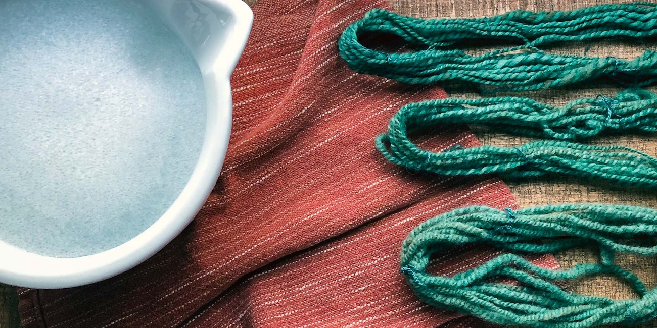 Yarn rests on a tea towel next to a bowl of soapy water.