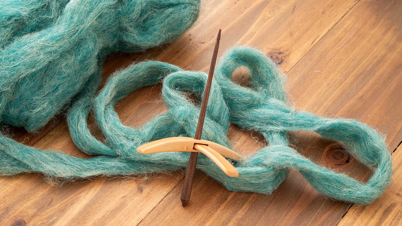 A cross-armed spindle with dark and light woods shown in front of blue-green roving on a wooden background.