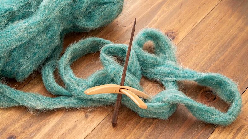 A cross-armed spindle with dark and light woods shown in front of blue-green roving on a wooden background.