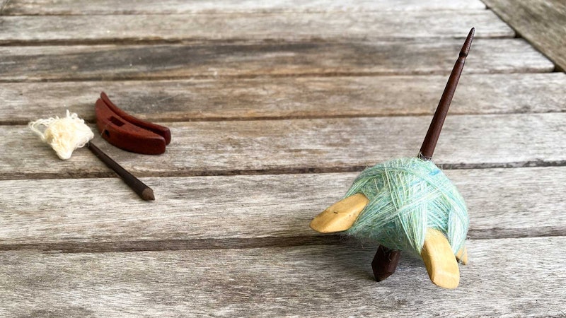 Two Turkish spindles. The spindle in the foreground is loaded with a cop of green yarn. The spindle in the background has been disassembled for travel.