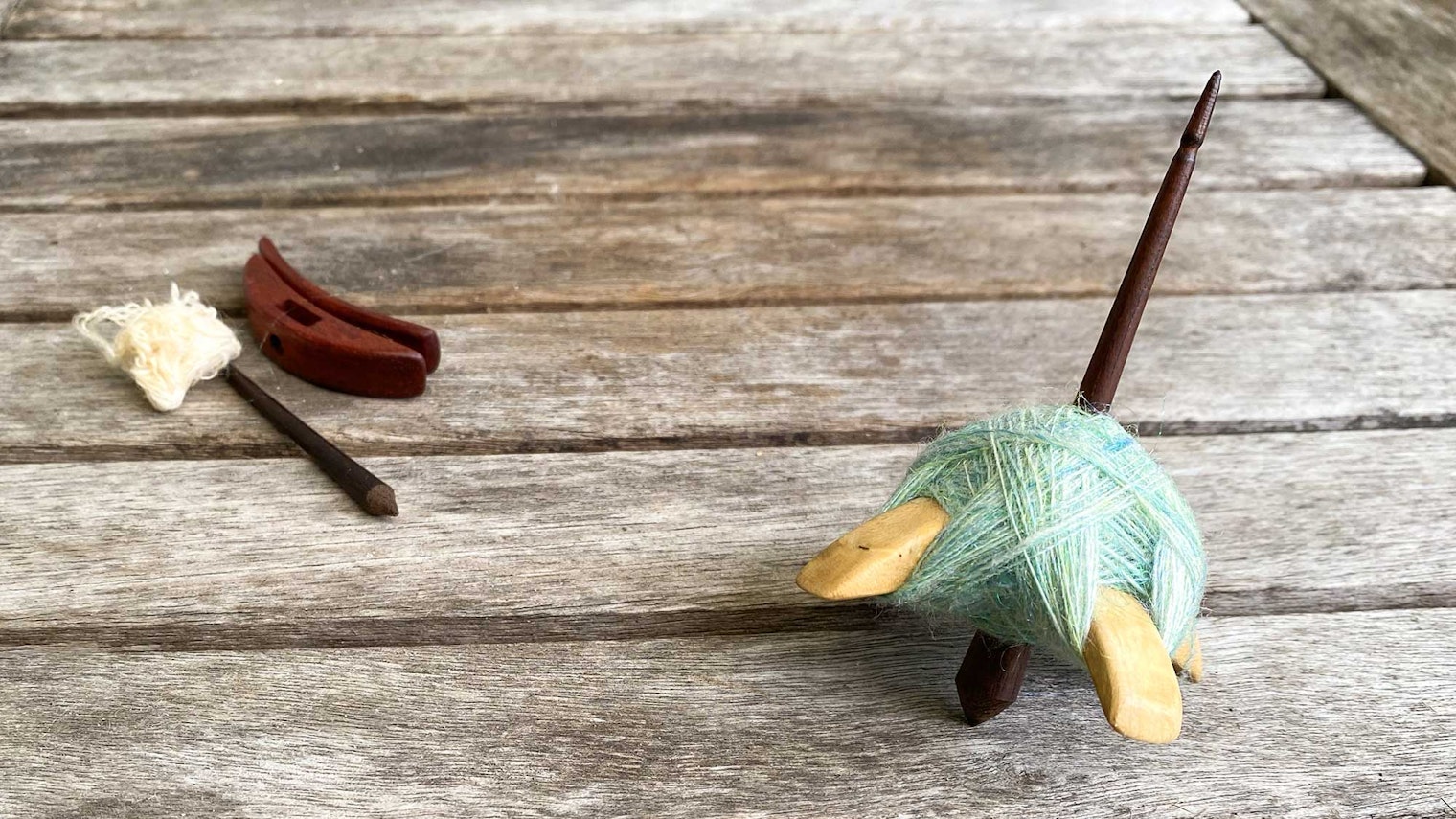 Two Turkish spindles. The spindle in the foreground is loaded with a cop of green yarn. The spindle in the background has been disassembled for travel.