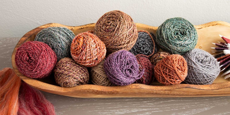 A long wooden bowl holds multicolored balls of yarn.