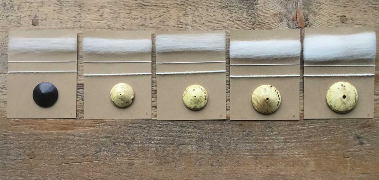Five dizzes against a wooden surface. Each diz is shown with the sliver pulled from it and the resulting yarn spun from the sliver.
